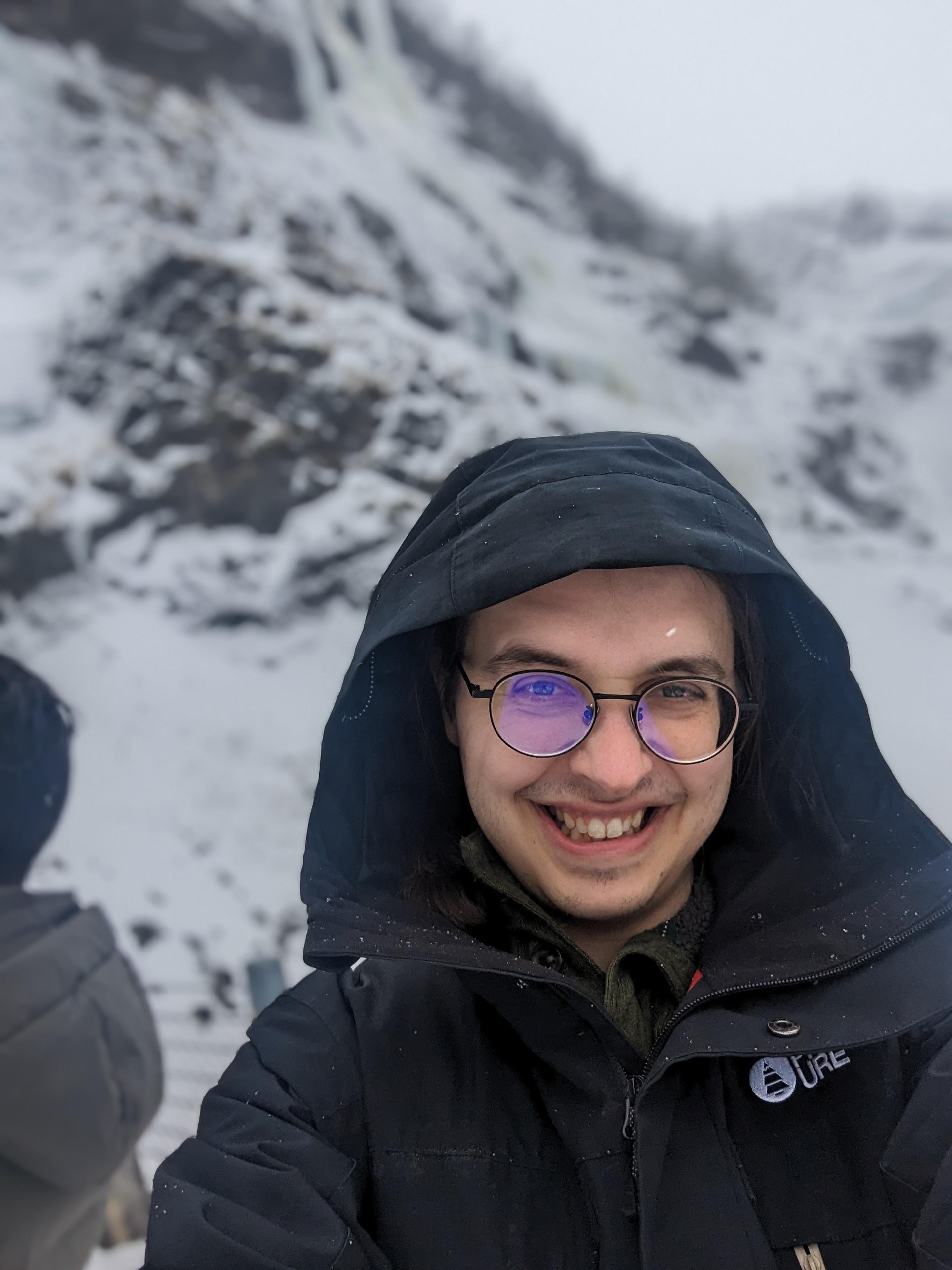 Photo of Joel Christiansen in a jacket in front of a mountain with snow on it.